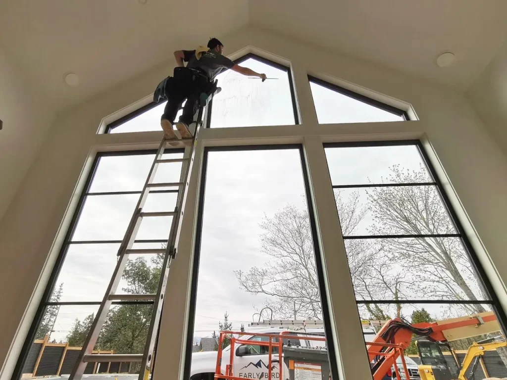 Early Bird Cleaning team member high up a ladder cleaning interior house windows